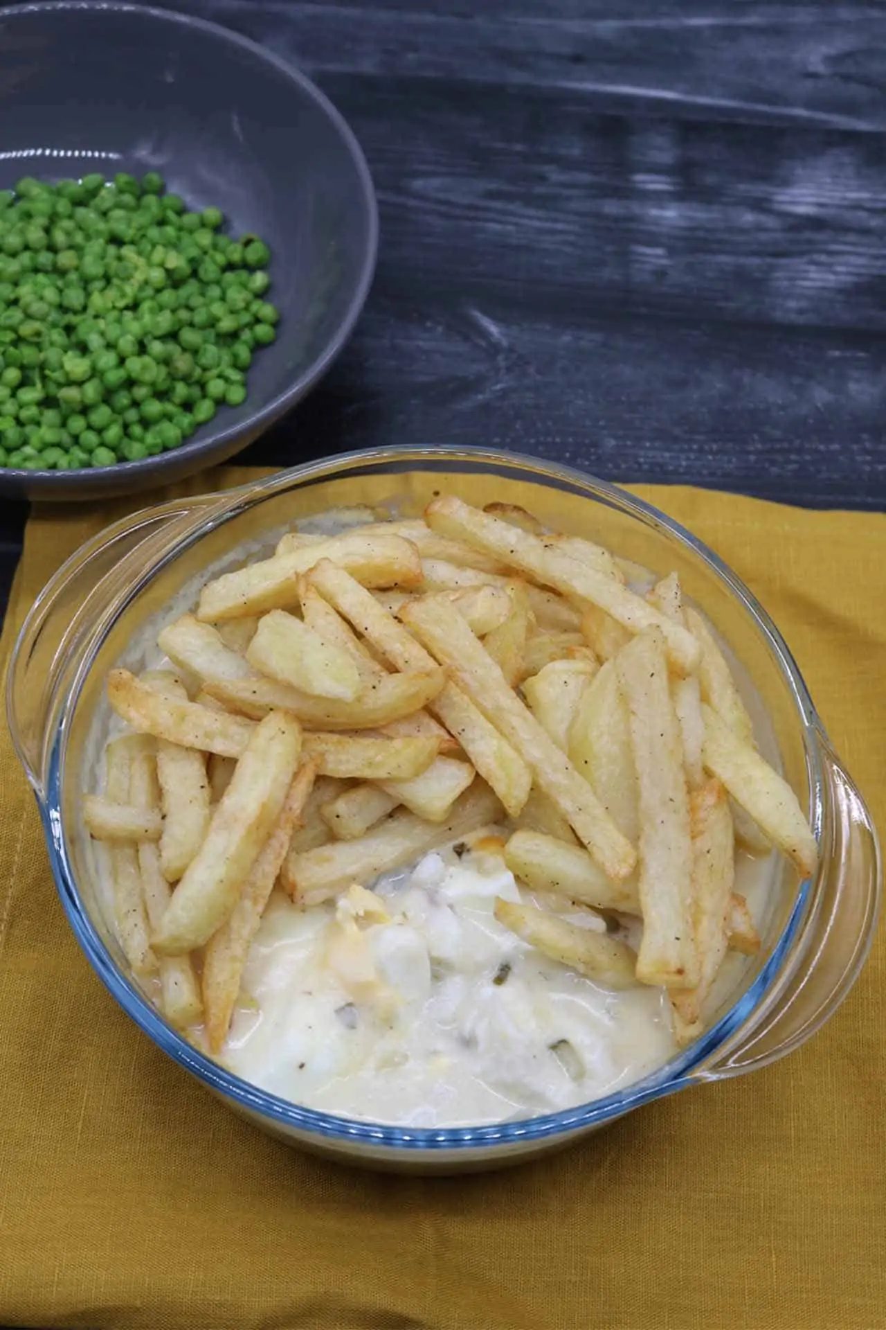 Fish and chip pie in a round glass serving bowl plus a bowl of peas on the side