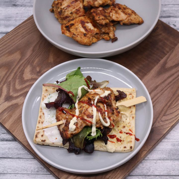 Chicken souvlaki on skewer in a flatbread with salad and sauces