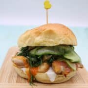 Piri piri crispy chicken in bun with cucumber sitting on wooden board