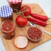 Chilli jam in jars with tomato and red chillis on wooden board