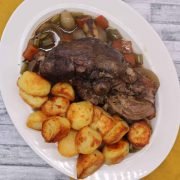 Slow cooker lamb shoulder on white oval serving dish with roast potatoes and vegetables
