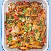 Dirty fries covered in cheese, spring onions, bacon and pepper in a rectangle oven tray