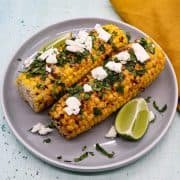 Grilled corn with feat coriander and lime wedges on grey plate