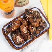 Honey and sriracha hot wings in a rectangle serving dish with yellow napkins, sriracha chilli mayo and honey on the side