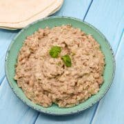Refried bean in green bowl with flour tortillas in background