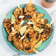 Sriracha lime chicken skewers in a bowl with lime wedges and sriracha chilli mayo in the background