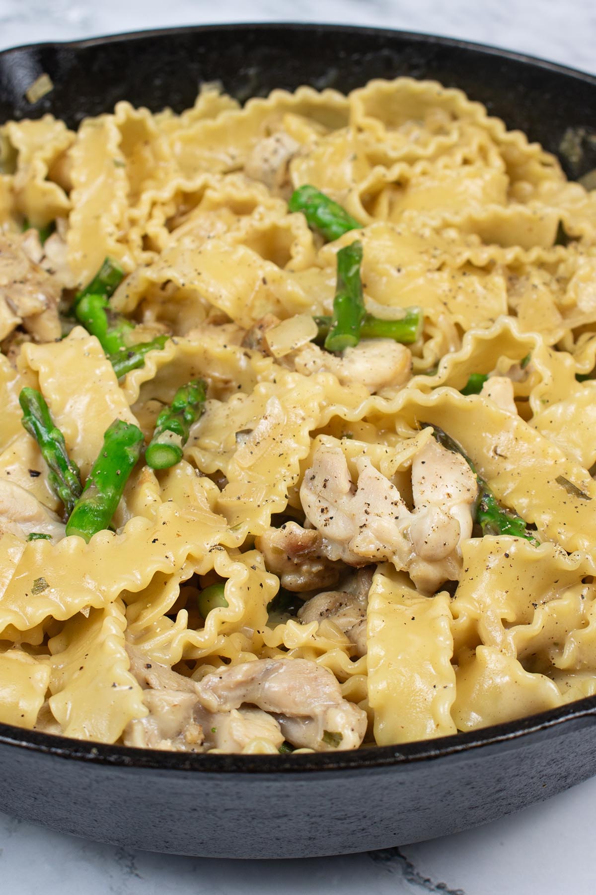 Close up of arragon chicken and asparagus mafalde in a large black skillet pan