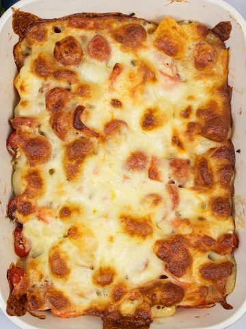 Baked gnocchi with tomatoes and mozzarella in rectangular baking dish with a bowl of salad on the side.