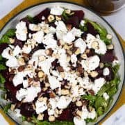 Beetroot, goat's cheese and rocket salad in serving bowl, garnished with chopped hazelnuts. Jug of dressing on the side.