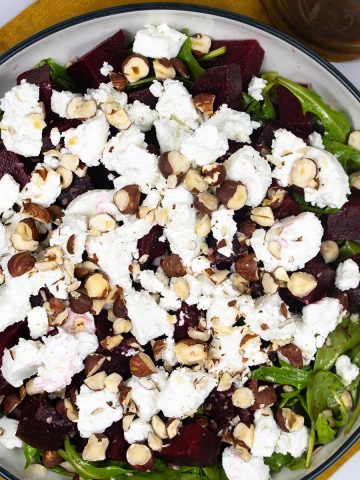 Beetroot, goat's cheese and rocket salad in serving bowl, garnished with chopped hazelnuts. Jug of dressing on the side.