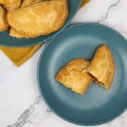 Chicken empanadas on teal plates with mustard napkin. One empanada cut in half on side plate