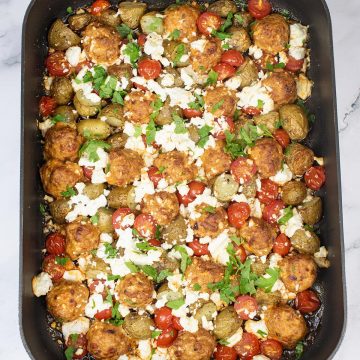 Chorizo meatball and feta traybake in large roasting tin with black and white towel on one end