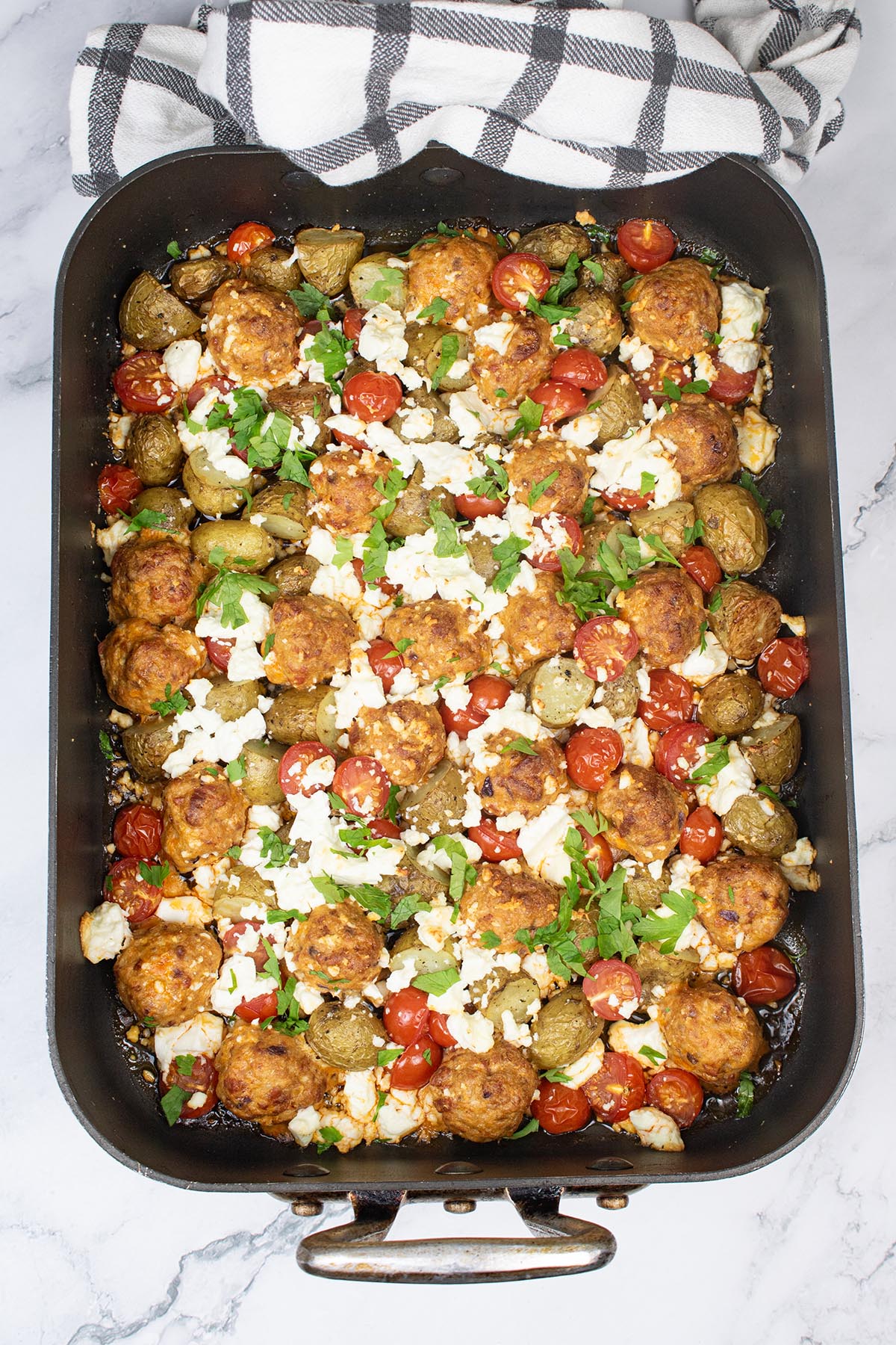 Chorizo meatball and feta traybake in large roasting tin with black and white towel on one end