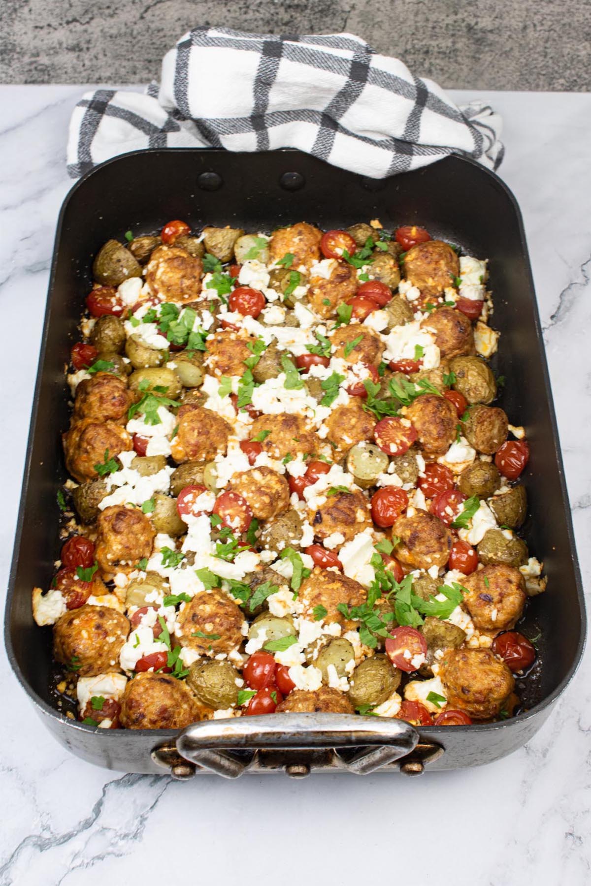 Chorizo meatball and feta traybake in large roasting tin with black and white towel at one end