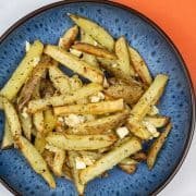 Feta and oregano fries in a blue patterned bowl with orange napkin in the background