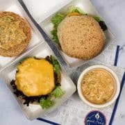 Two double smash cheeseburgers in burger boxes with a small dish of burger sauce on the side