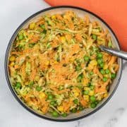 Carrot salad in a serving bowl with spoon and orange napkin in the background