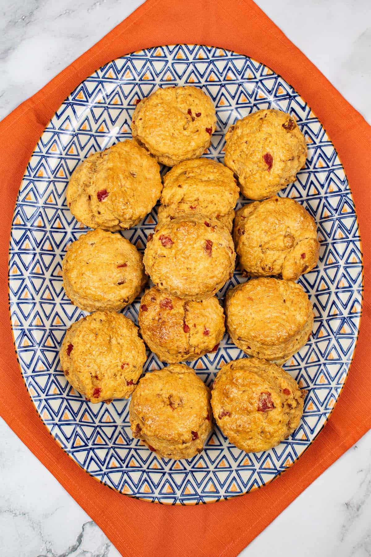 Chorizo, red pepper and paprika scones on a blue and orange patterned platter on top of an orange napkin.
