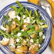 Spring potato salad in a blue and white serving bowl with tongs and mustard napkin on the side.