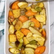 Roasted root vegetables in a white rectangle serving dish with spoon. Green and white checked towel in the background.