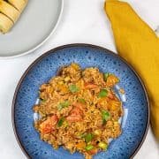 Portion of spicy sausage rice in a blue patterned bowl with garlic bread on a grey side plate, and mustard napkin on the side.