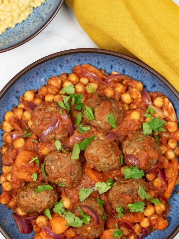 Lamb meatball tagine in a blue patterned bowl, with a bowl of couscous and mustard napkin on the side.