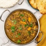 Close up of quick lamb dhansak in a balti dish with a dish of rice and plate of naan bread on the side.