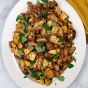 Roasted chicken wings with roast potatoes, oregano and garlic on a white platter with mustard napkin on the side.