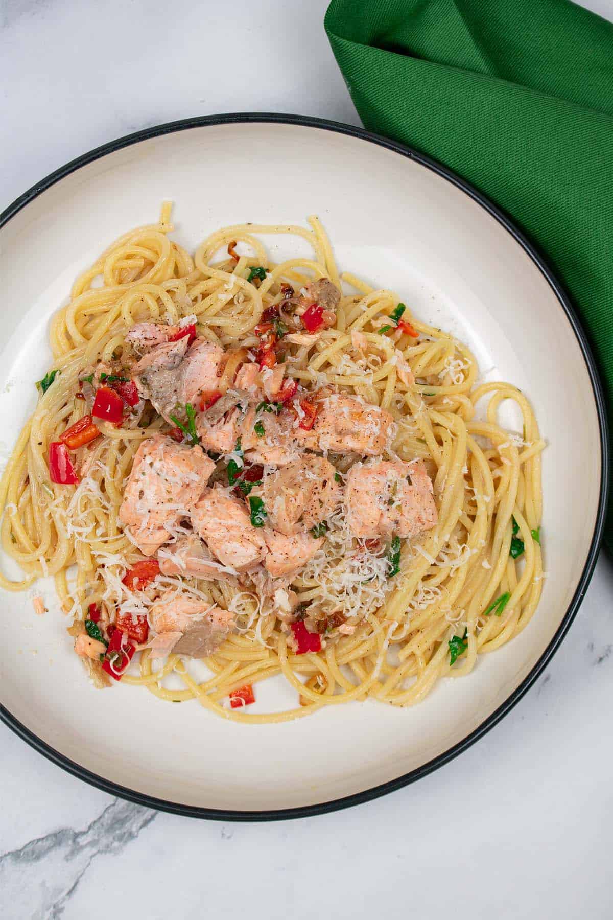 Spaghetti with hot smoked salmon, chilli and white wine in a black and cream bowl with a green napkin on the side.