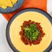 Chorizo dip made in Thermomix in a blue patterned serving bowl, with a matching bowl of tortilla crisps and orange napkin in the background.