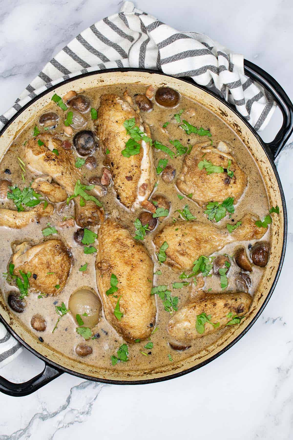 Coq au riesling in a round casserole with a black and white striped towel around the handles.