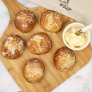 Crusty white dinner rolls on a board with a dish of butter with butter knife. Bread bag in the background.