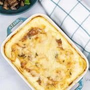 Dauphinoise potatoes in a rectangle baking dish with a bowl of easy garlic mushrooms and a checked teal and white towel on the side.
