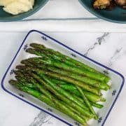 Easy sautéed asparagus in a blue and white rectangle pattered dish with teal bowls of horseradish mash and garlic mushrooms in the background.