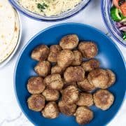 Greek lamb meatballs made in the Thermomix in a blue bowl with Greek rice with spinach, Greek salad and flatbreads on the side.