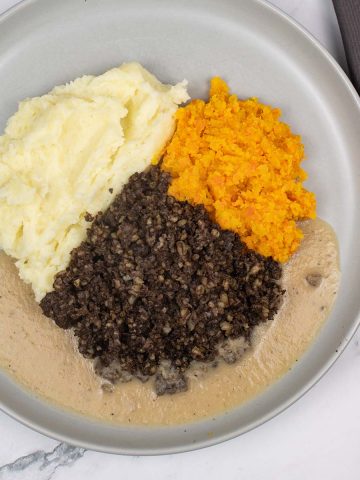 Haggis, neeps, tatties and whisky sauce on a grey dinner plate and charcoal napkin on the side.