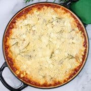 Lamb and rosemary mac with pecorino and feta crumb topping in a large casserole with sprigs of rosemary, salt and pepper and a green napkin on the side.