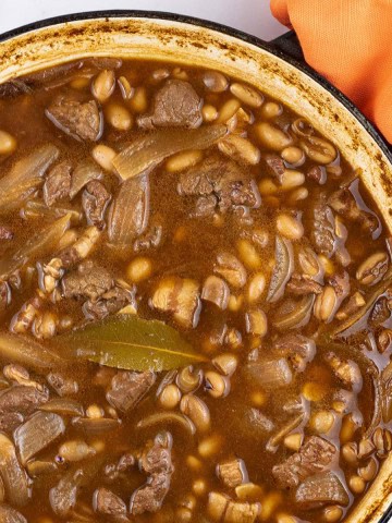 Beef and boston baked beans in large round casserole with orange napkin on the handle.