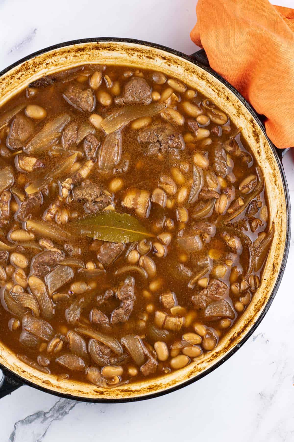 Beef and boston baked beans in large round casserole with orange napkin on the handle.