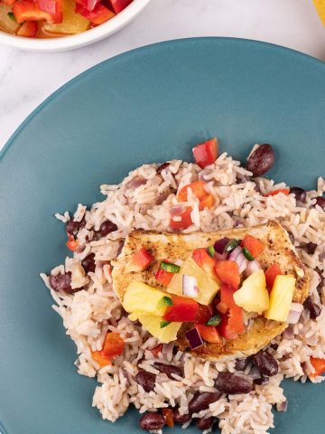 Cajun turkey steak with pineapple salsa and kidney bean rice on a teal plate. A bowl of salsa and mustard napkin on the side.