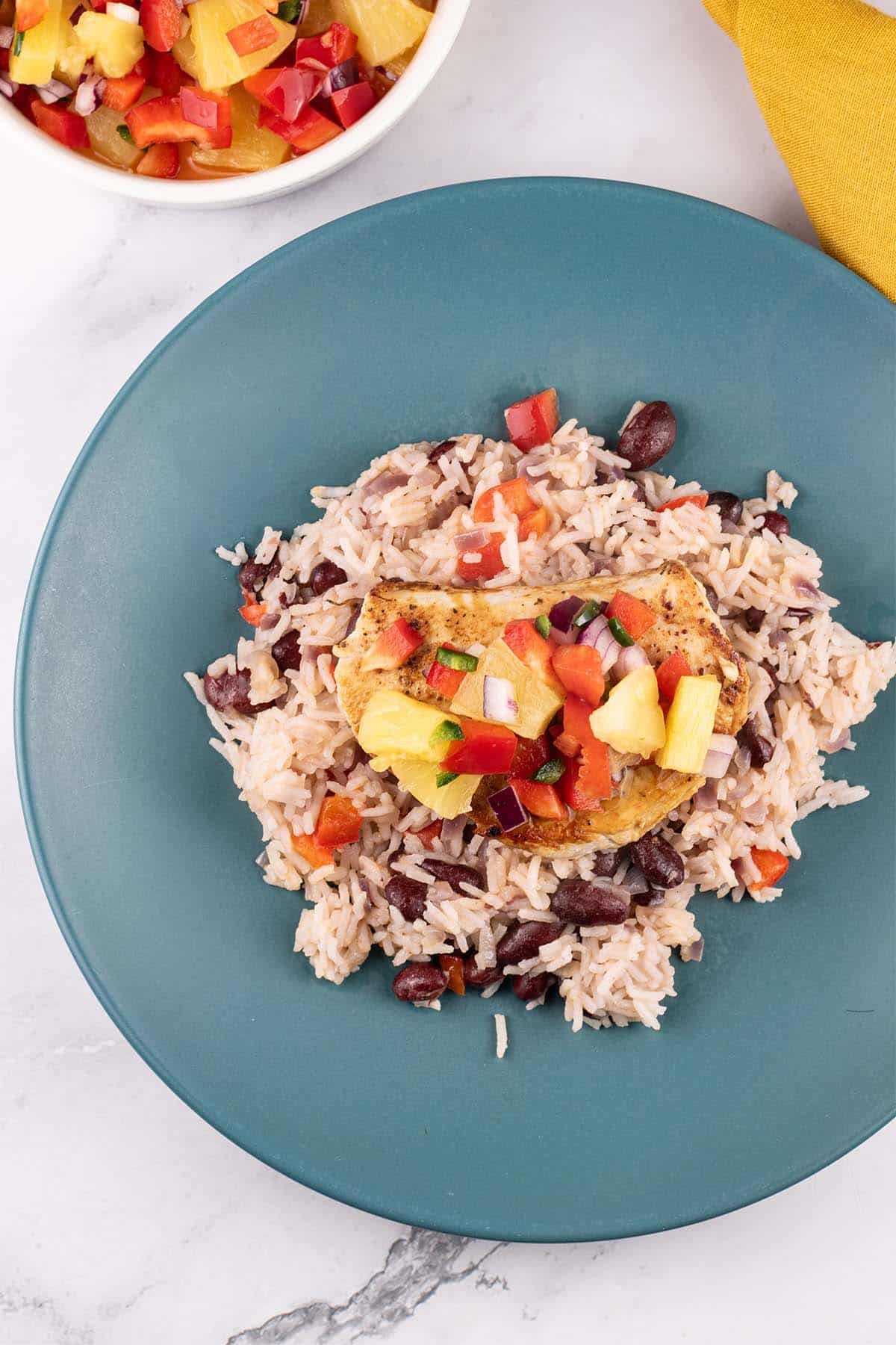Cajun turkey steak with pineapple salsa and kidney bean rice on a teal plate. A bowl of salsa and mustard napkin on the side.