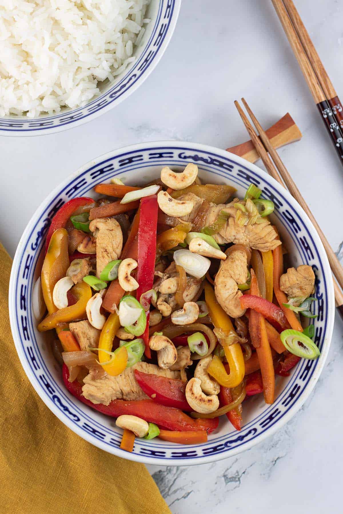 Chicken and cashew nut stir-fry in an oriental bowl with a bowl of jasmine rice and chopsticks on the side.