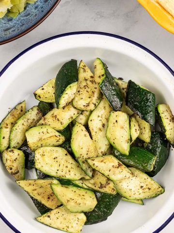 Easy air fryer courgettes in a round blue rimmed white enamel dish with a bowl of cabbage and a pie in the background.