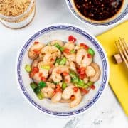 Easy salt and chilli pepper prawns in a blue and white oriental bowl, with a bowl of dipping sauce and jar of Chinese seasoning in the background.