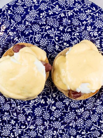 Eggs benedict with quick hollandaise sauce on a blue and white patterned dinner plate, with a small jug of sauce on the side.