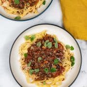 2 pasta bowls of lamb, tomato and oregano ragu with tagliatelle and a mustard napkin on the side.