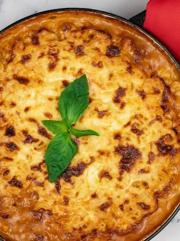 Mac 'n' cheese with rich beef ragu in a large round casserole with red napkin on the handle.