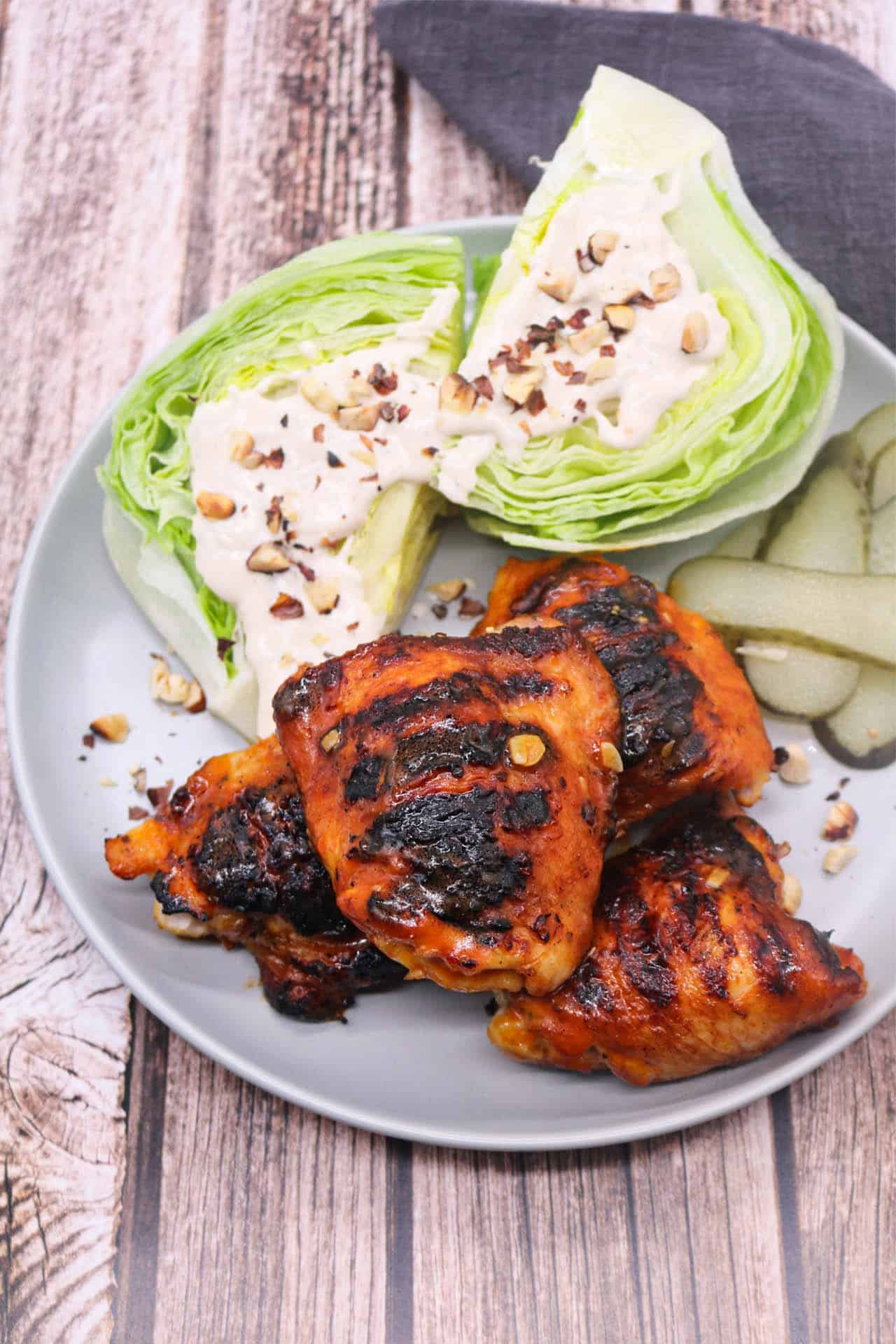 BBQ buffalo chicken thighs with wedged ranch salad on a grey dinner plate, with a grey napkin on the side.
