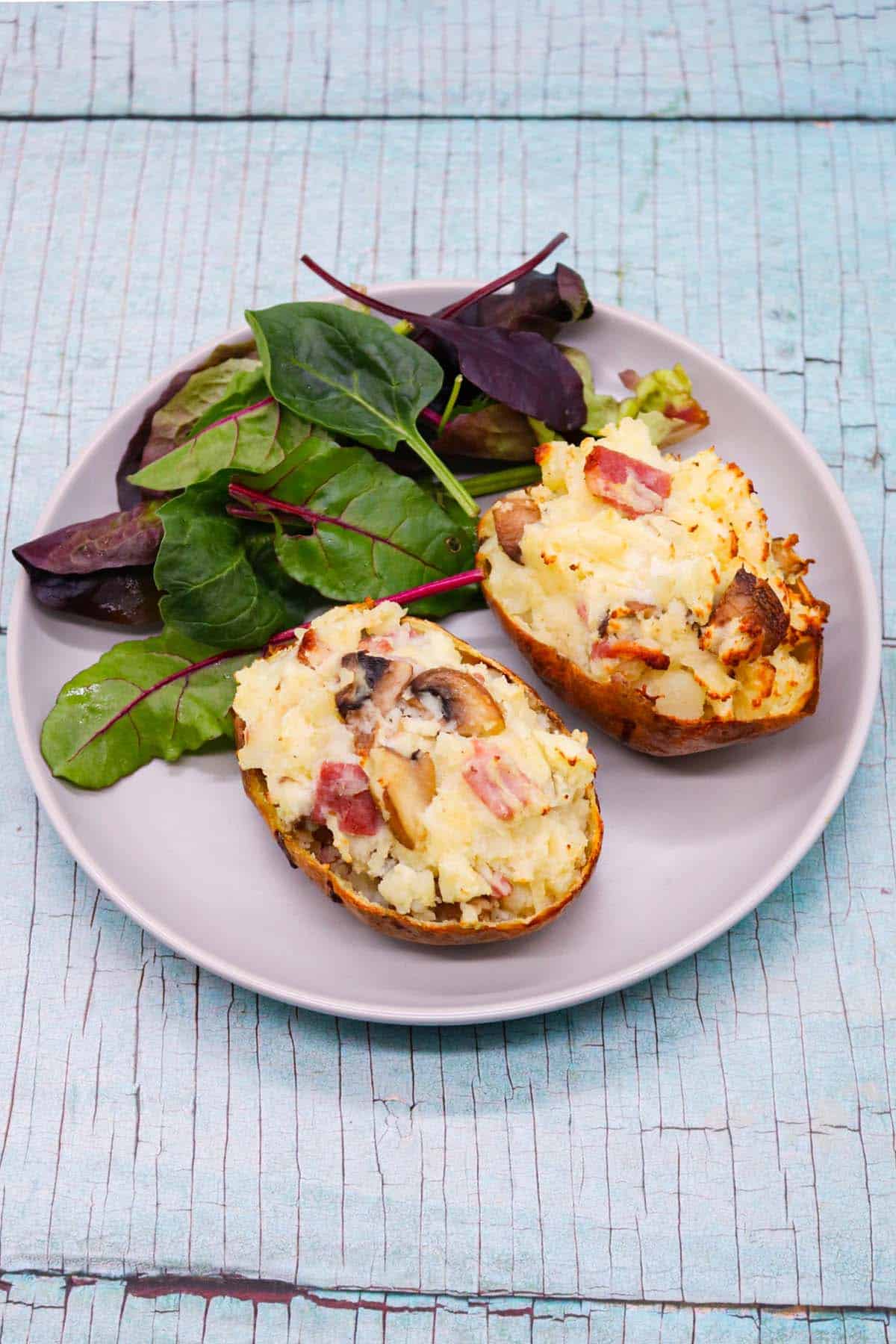 Bacon and mushroom baked potato on grey plate with salad leaves