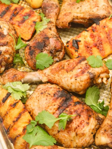 Cajun chicken with charred pineapple wedges on a large baking tray, garnished with coriander.